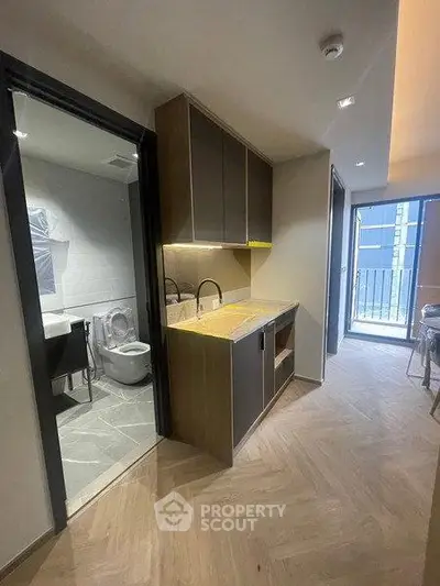 Modern apartment interior with compact kitchen and bathroom, featuring sleek cabinetry and herringbone flooring.