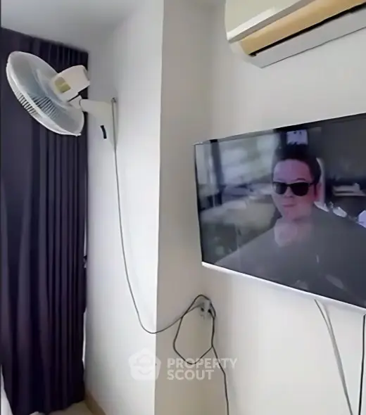Modern living room with wall-mounted TV and air conditioning unit, featuring sleek curtains and a fan.