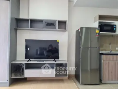 Modern living area with sleek TV unit and stainless steel fridge in compact kitchen.