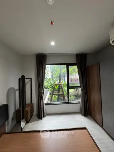 Spacious bedroom with large window and garden view, featuring modern furnishings and ample natural light.