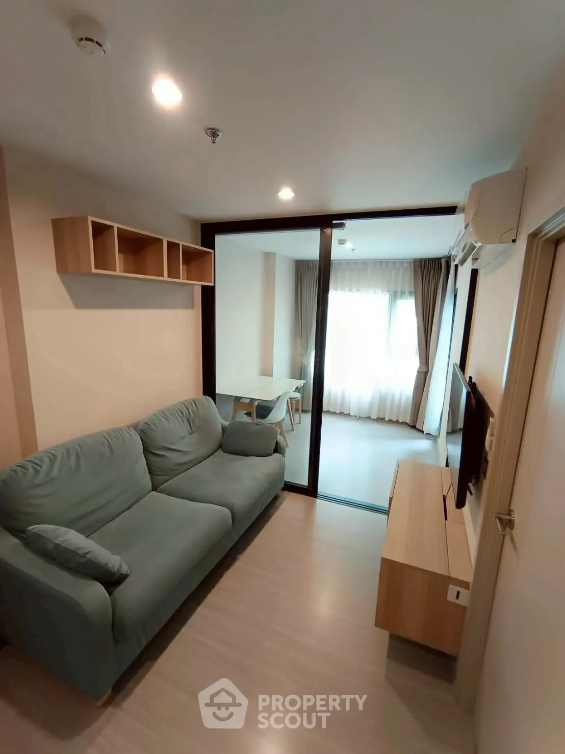 Modern living room with cozy sofa and TV, featuring a glass partition to a bright study area.