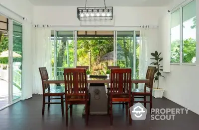 Elegant dining area with garden view, featuring wooden table and chairs, large windows, and lush greenery.