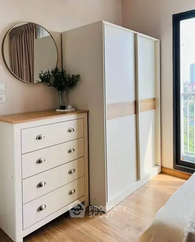 Modern bedroom with sleek wardrobe and dresser, featuring a round mirror and balcony view.