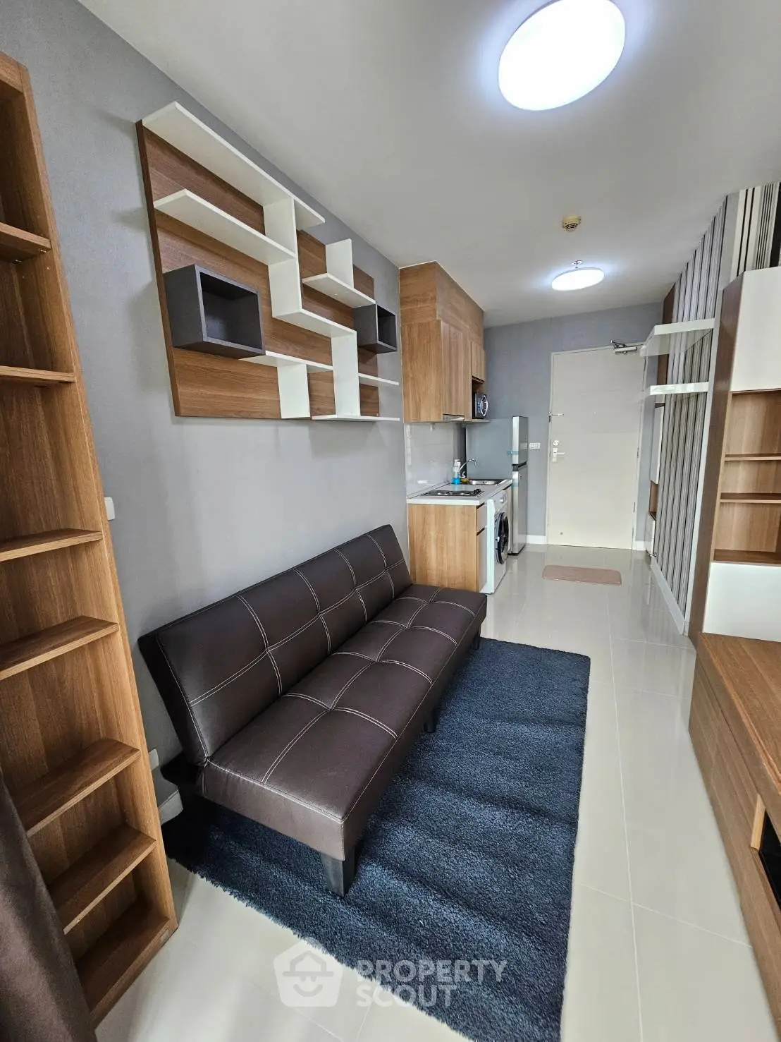 Modern living room with stylish shelving and compact kitchen in open layout apartment.