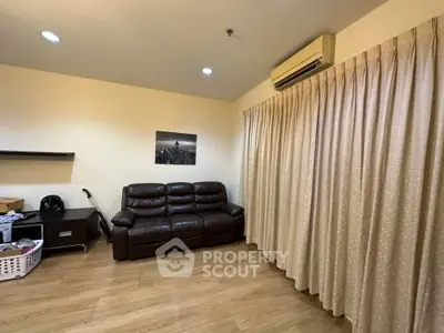 Cozy living room with leather sofa and air conditioning, featuring wooden flooring and elegant curtains.
