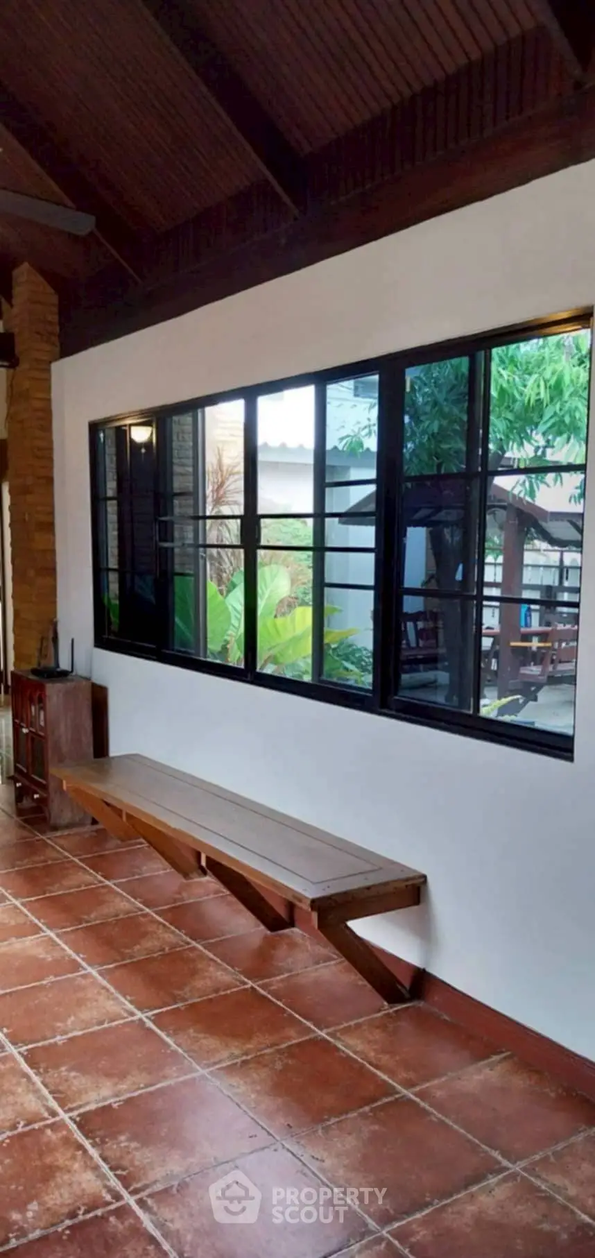 Charming rustic patio with terracotta tiles and wooden bench, overlooking lush garden view.