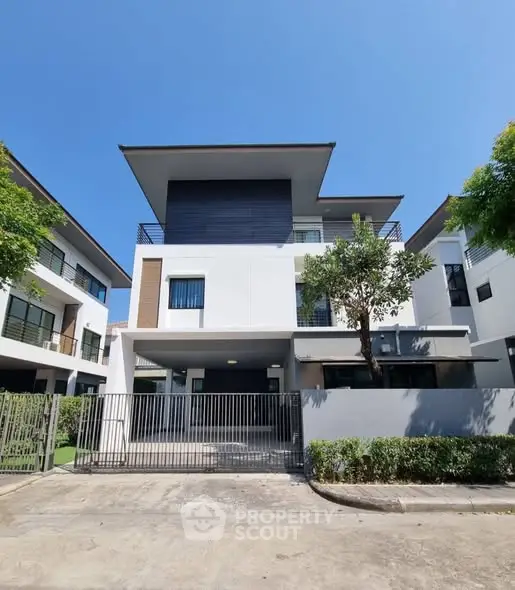 Modern three-story house with sleek design and spacious balcony under clear blue sky.