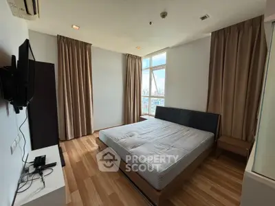 Spacious bedroom with large window and modern furnishings in a high-rise apartment.