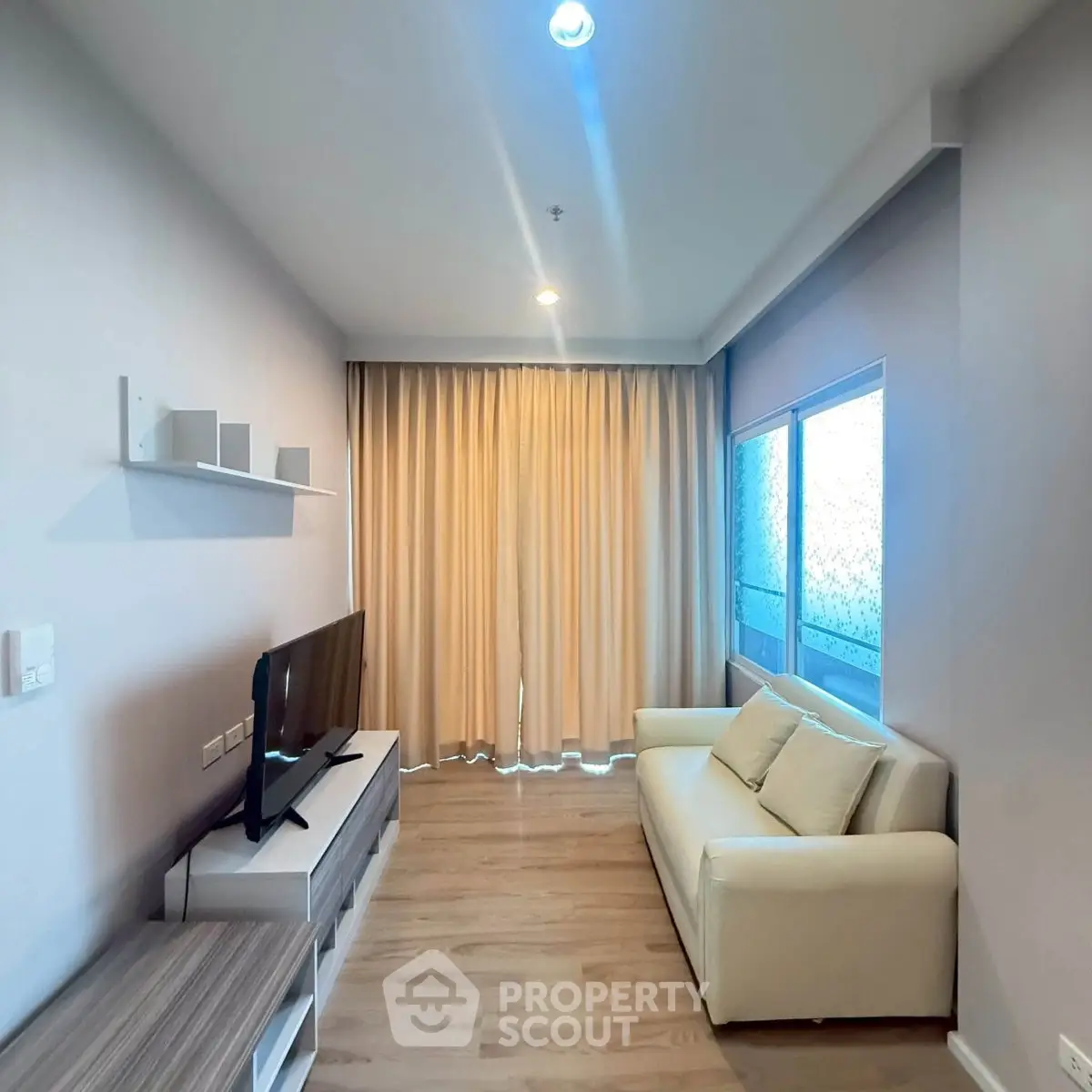 Modern living room with cozy sofa and large TV, featuring elegant curtains and sleek wooden flooring.