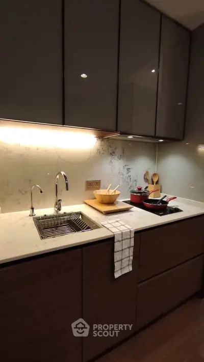 Modern kitchen with sleek cabinetry and under-cabinet lighting, featuring a stylish sink and cooking essentials.
