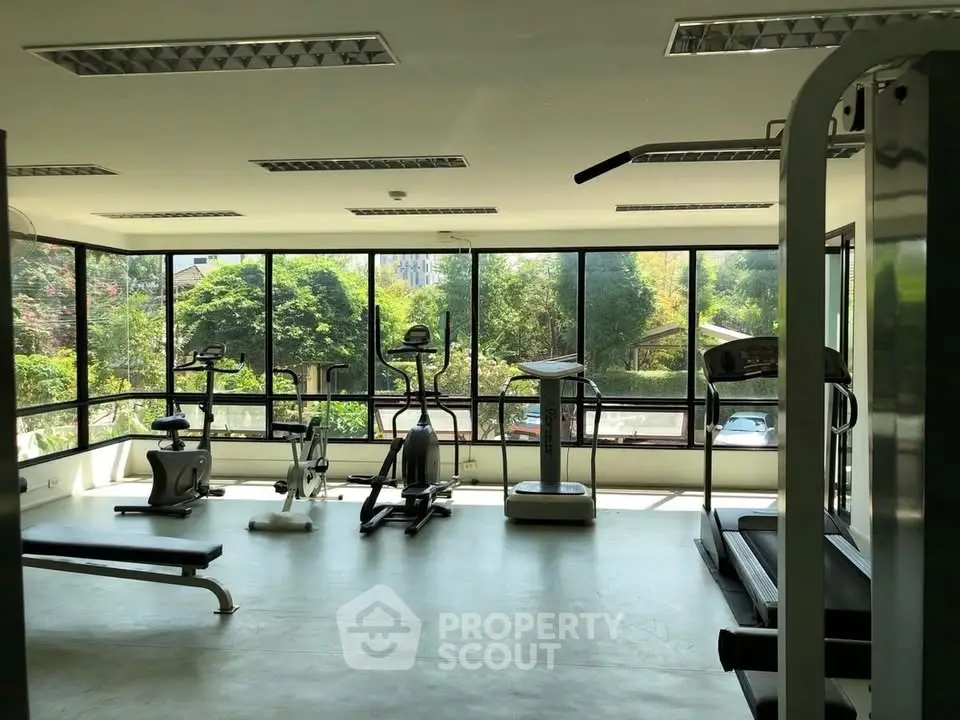 Spacious gym with modern equipment and large windows offering lush garden views.