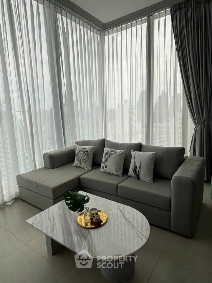 Modern living room with elegant gray sofa and marble coffee table, featuring floor-to-ceiling windows with city view.