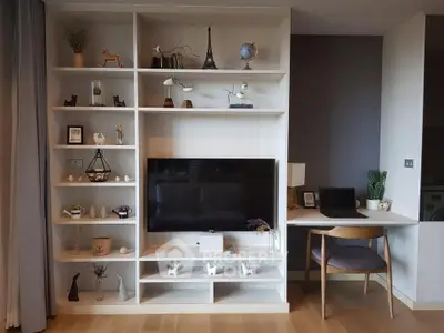 Modern living room with stylish shelving and workspace, featuring a flat-screen TV and decorative items.