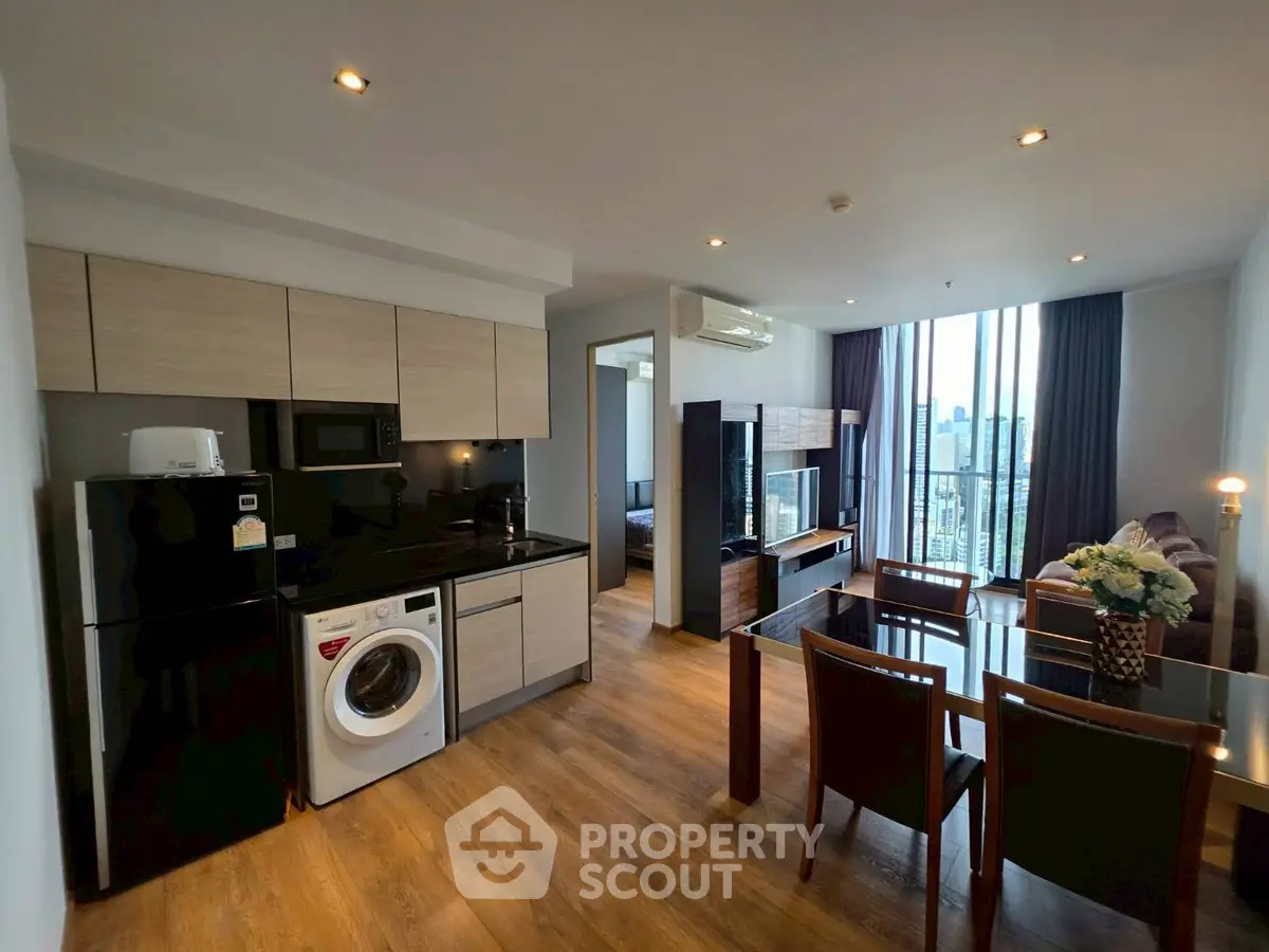 Modern open-plan living room with kitchen and dining area, featuring wooden flooring and city view.