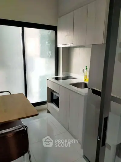 Modern compact kitchen with sleek cabinetry and dining area, featuring a minimalist design and natural light.