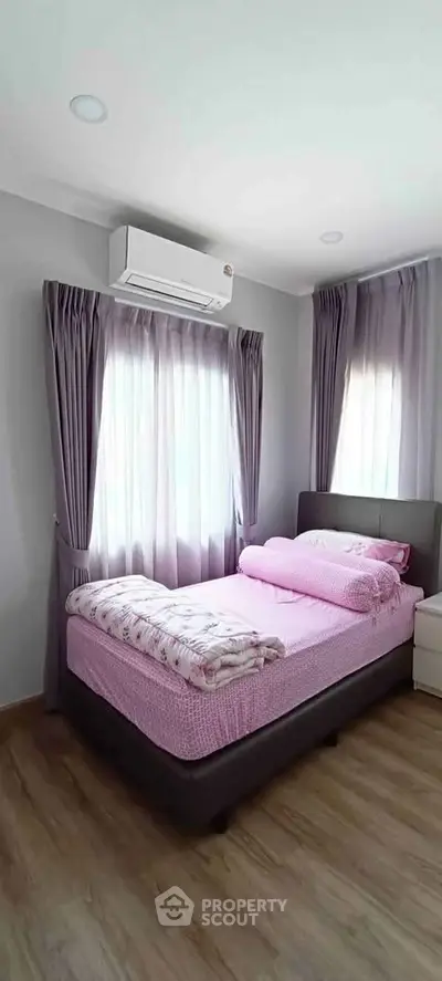 Cozy bedroom with pink bedding, air conditioning, and natural light from two windows.