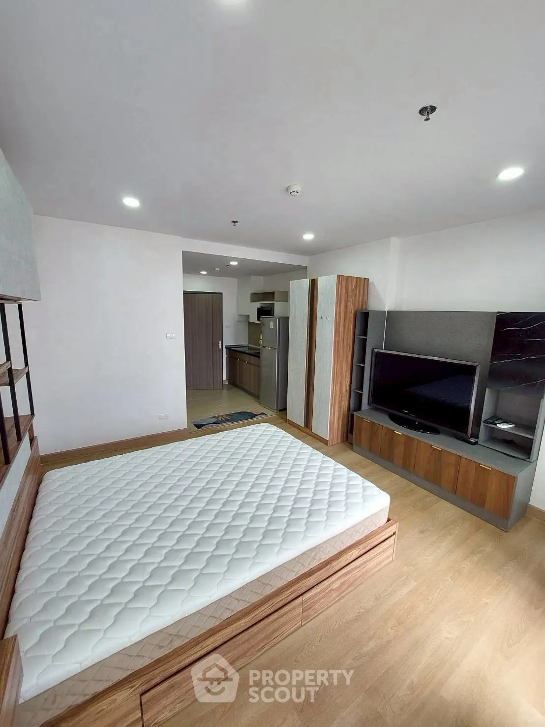Modern bedroom with wooden flooring, large TV, and stylish furniture in a contemporary apartment.
