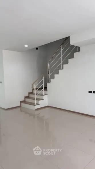 Modern minimalist staircase in a spacious open-plan living area with sleek tile flooring.