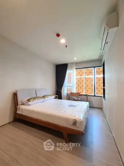 Modern bedroom with stylish wooden bed and large window offering natural light.