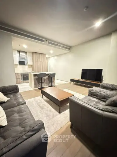 Modern living room with open kitchen, leather sofas, and sleek TV setup.