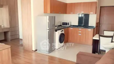 Modern kitchen with wooden cabinets, fridge, and washing machine in open layout.