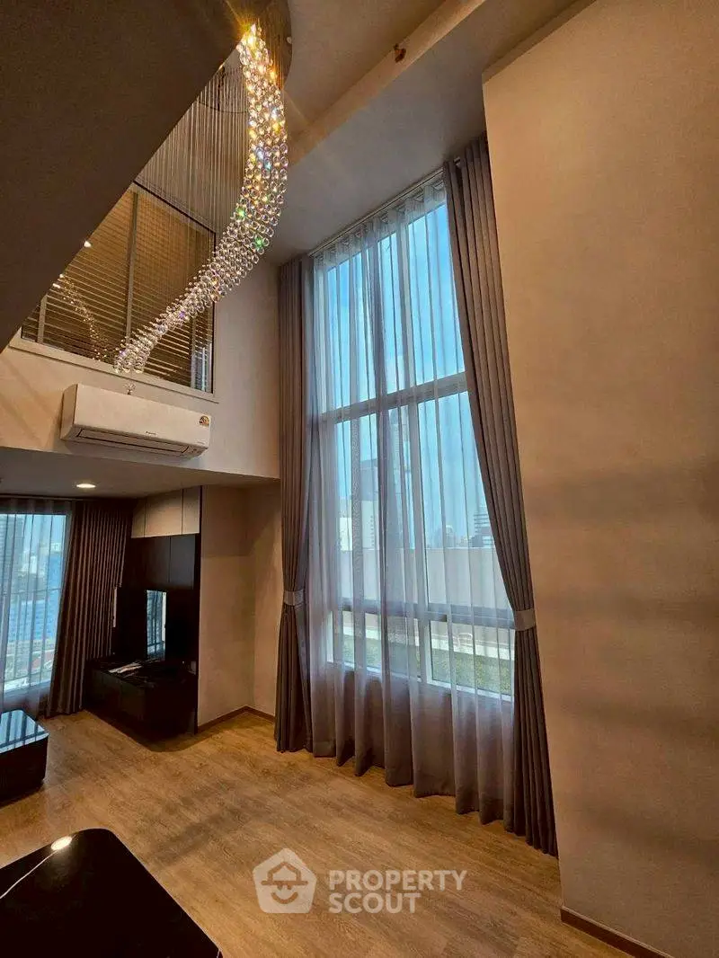 Luxurious high-ceiling living room with elegant chandelier and floor-to-ceiling windows.