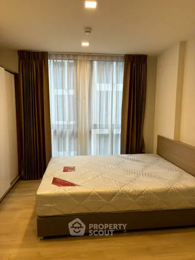Modern bedroom with large window and stylish curtains, featuring a comfortable bed and wooden flooring.