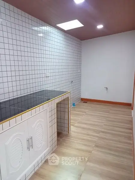 Spacious kitchen with tiled walls and wooden flooring, perfect for modern living.
