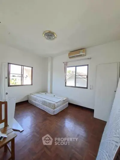 Spacious bedroom with natural light and wooden flooring, featuring a single bed and air conditioning.