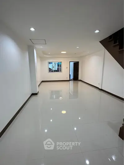 Spacious empty room with glossy tiled floor and staircase, ideal for customization.