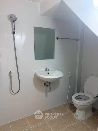 Modern bathroom with sleek fixtures and under-stair design, featuring a shower, sink, and toilet.