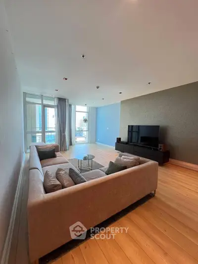 Spacious modern living room with large sofa and city view balcony.
