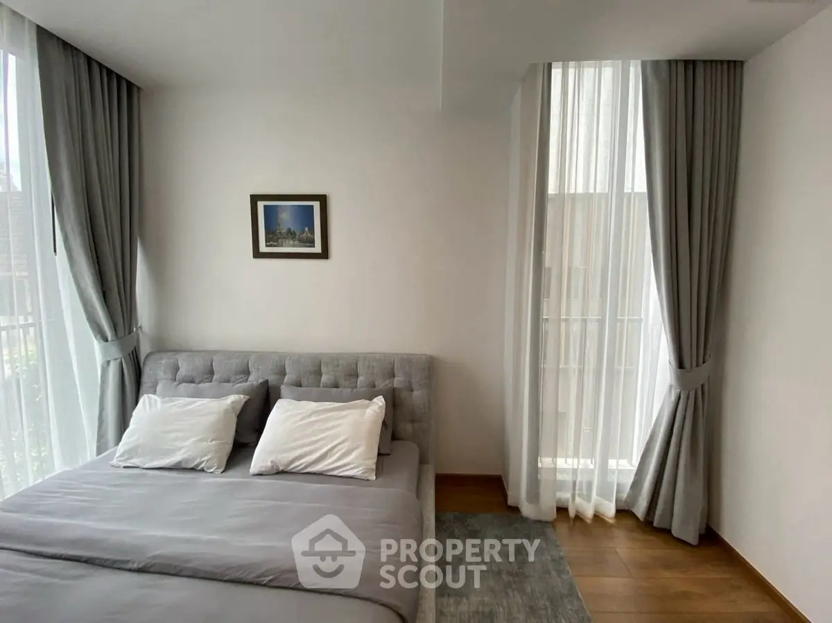 Elegant bedroom with modern decor, large windows, and soft gray curtains in a stylish apartment.