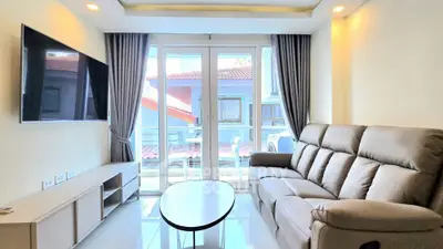 Modern living room with sleek sofa, wall-mounted TV, and large windows offering natural light.