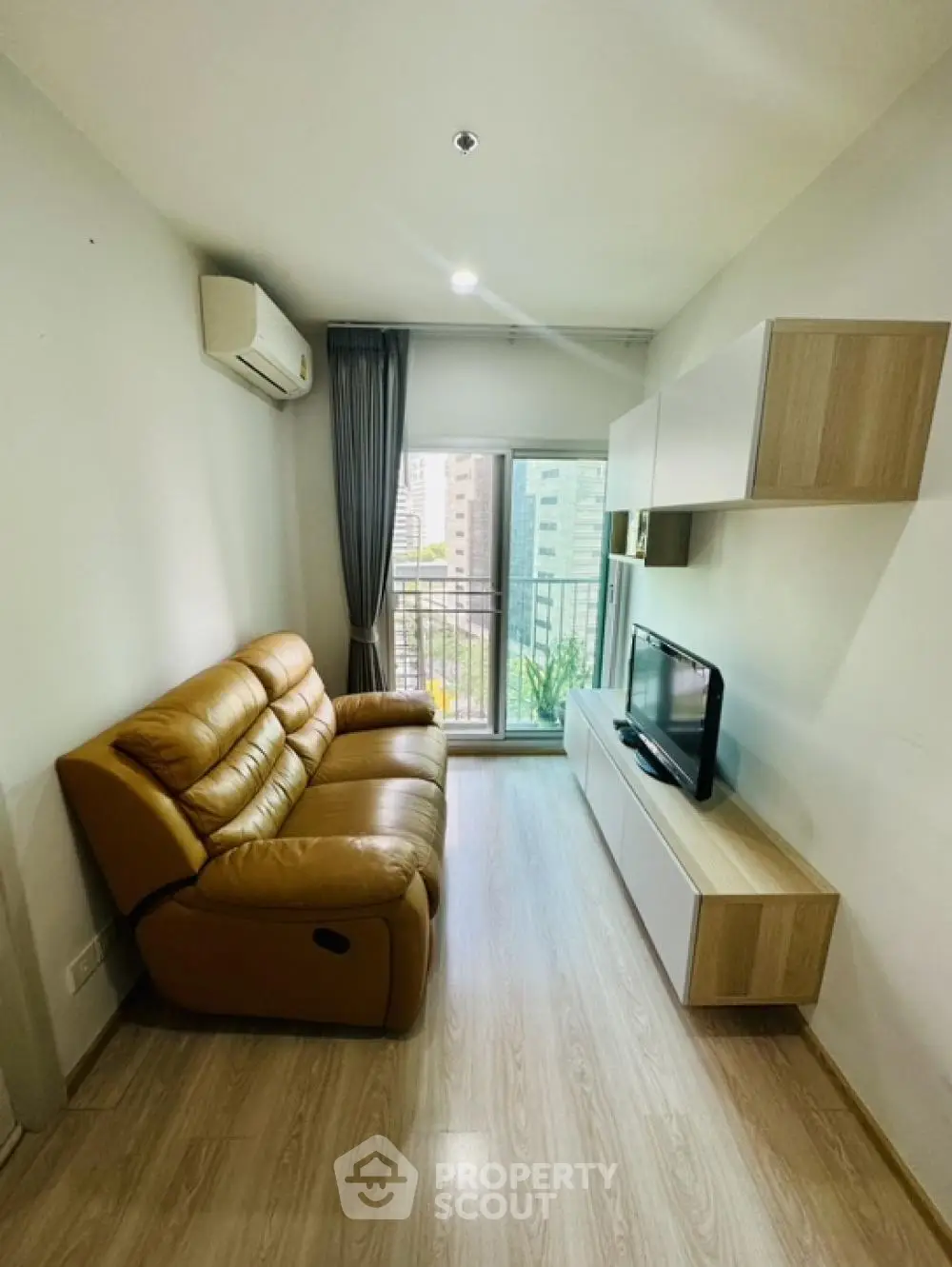Cozy modern living room with plush leather sofa, sleek wall-mounted shelves, and ample natural light streaming in from the balcony, perfect for urban living.
