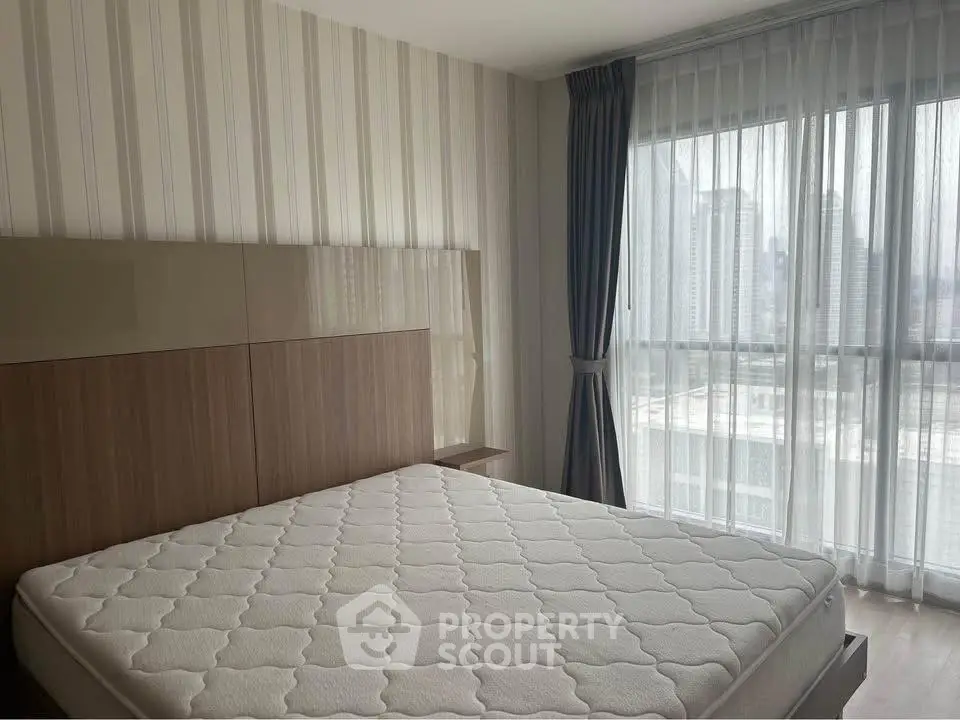 Modern bedroom with large window and city view, featuring a stylish bed and elegant curtains.