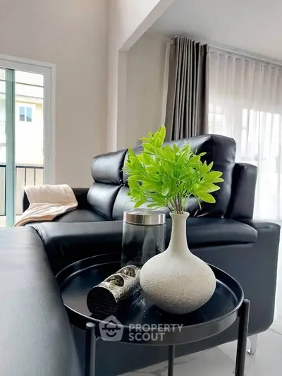 Modern living room with sleek black leather sofa and stylish decor in a bright, airy space.