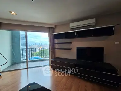 Modern living room with balcony and city view, featuring sleek black furniture and wooden flooring.