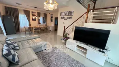 Spacious modern living room with elegant decor and open dining area, featuring a stylish staircase and large TV.