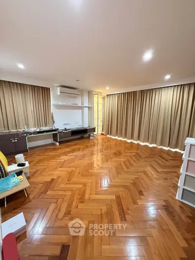 Spacious living room with elegant parquet flooring and modern lighting, perfect for family gatherings.