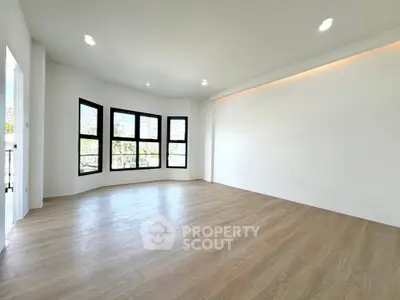 Spacious empty room with large windows and wooden flooring, perfect for customization.