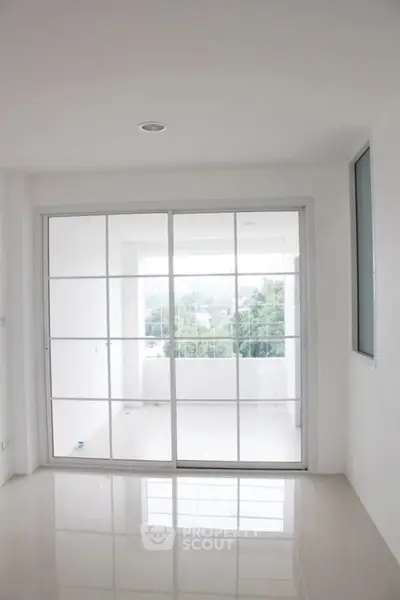 Spacious modern living room with large sliding glass doors leading to a bright balcony with a scenic view.