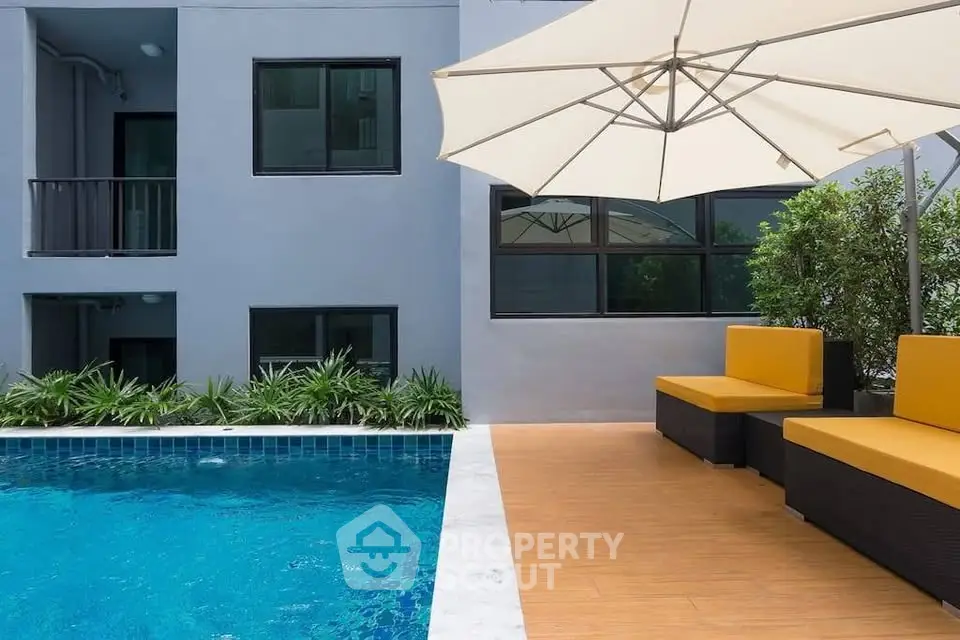 Modern apartment poolside with stylish seating and umbrella, perfect for relaxation.