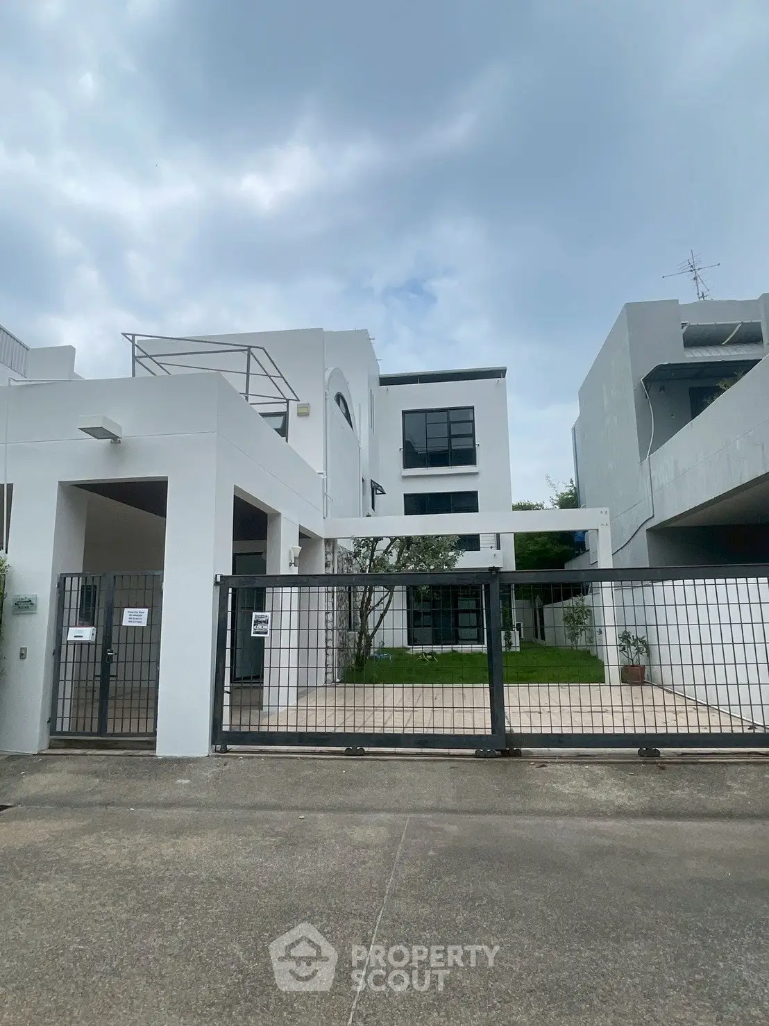 Modern white building with gated entrance and lush greenery, perfect for urban living.