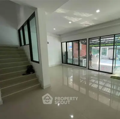 Spacious modern living room with large windows and sleek staircase, perfect for natural light lovers.