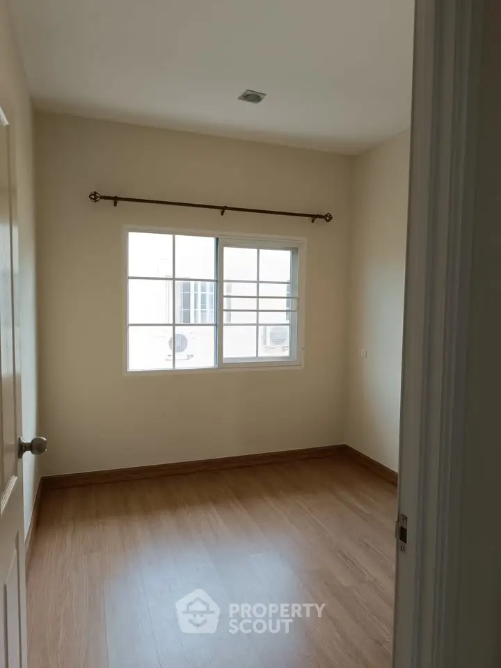 Bright empty room with wooden flooring and large window, perfect for customization.