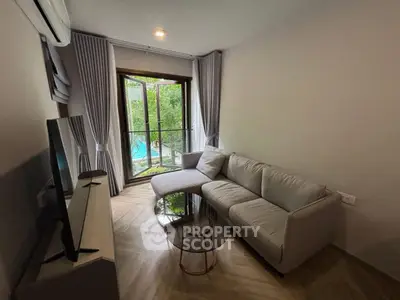 Cozy living room with modern sofa and glass coffee table, overlooking lush garden view.