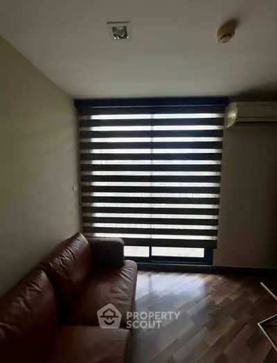 Cozy living room with modern blinds and leather sofa, featuring wooden flooring and air conditioning.