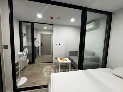 Modern studio apartment with glass partition, cozy living area, and compact kitchen.