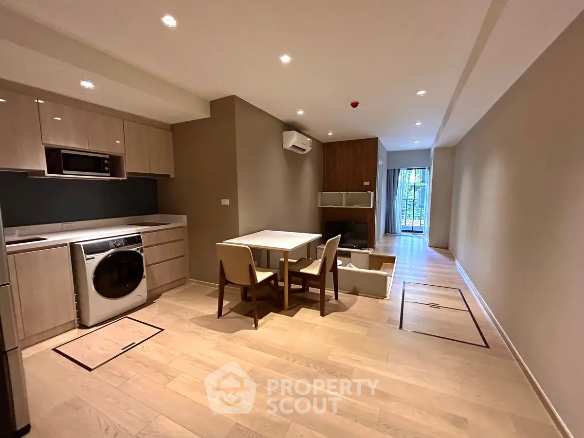 Modern open-plan living room with kitchen and dining area, featuring wooden flooring and natural light.